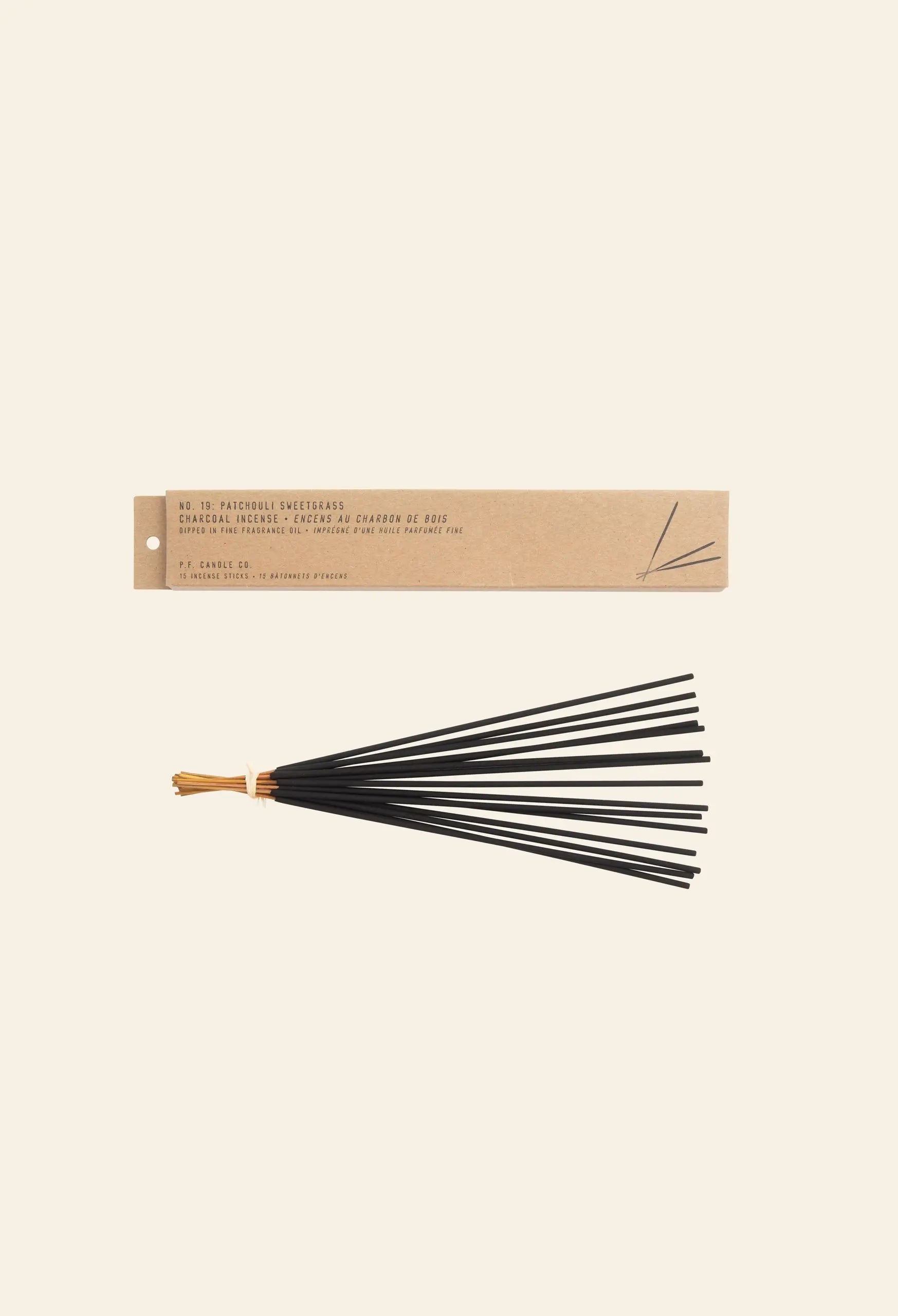 A brown rectangular box of P.F. Candle Co. Classic Incense rests above a bundle of black incense sticks tied with tan string, evoking teakwood and leather notes, set against a cream background.