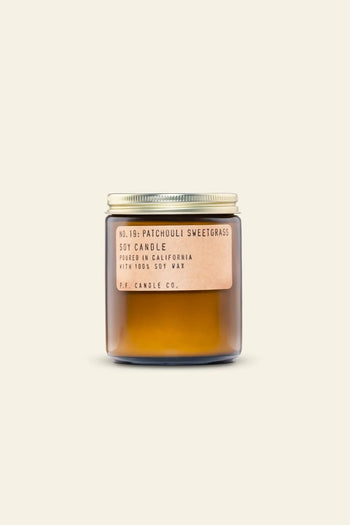 The P.F. Candle Co. No. 19 Patchouli Sweetgrass 7.2 oz Soy Candle features a brown glass jar, gold metal lid, and tan label—crafted with clean-burning soy wax for a calming atmosphere. Shown on a plain beige background.