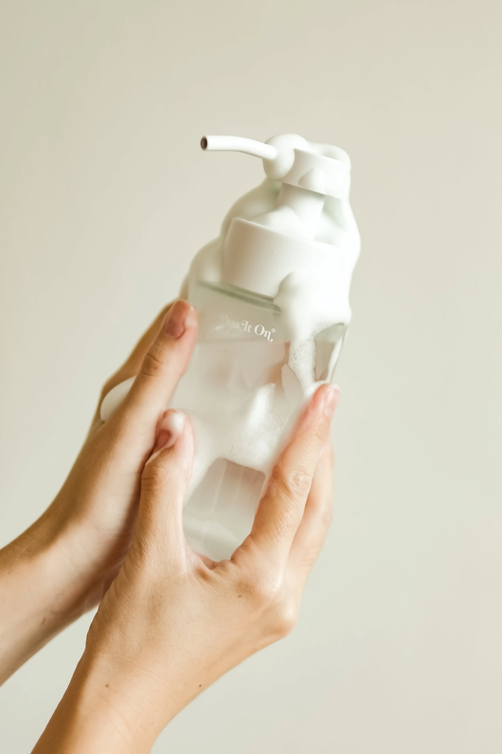 Two hands hold a Pass It On 0.02 Refillable Hand Wash bottle in Marine Moss, covered in white foam against a light background. Set includes 3 bottles from Pass It On, combining freshness with eco-friendly refillable design.