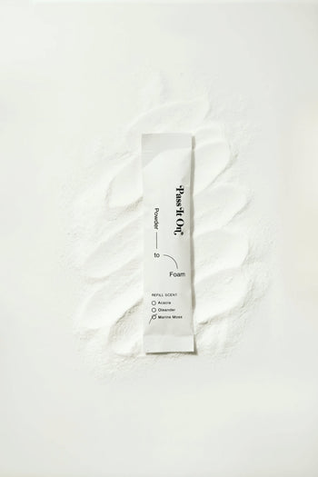 A white sachet labeled Pass It On 0.02 Refillable Hand Wash Set, Single Pack - Marine Moss rests on white powder, highlighting its sustainable, refillable design by Pass It On against a clean, minimal background.