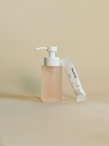 The Pass It On 0.02 Refillable Hand Wash Set, Single Pack - Oleander features a clear pump bottle with light pink liquid and white dispenser beside a small white botanically-derived powder packet, both with minimalist branding.
