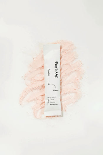 A Pass It On 0.02 Refillable Hand Wash Set, Single Pack - Oleander by Pass It On rests on a mound of light pink botanical powder. The packet highlights refill scents for sustainable hand hygiene: Acacia, Osmanthus, Gardenia, Marine Musk.