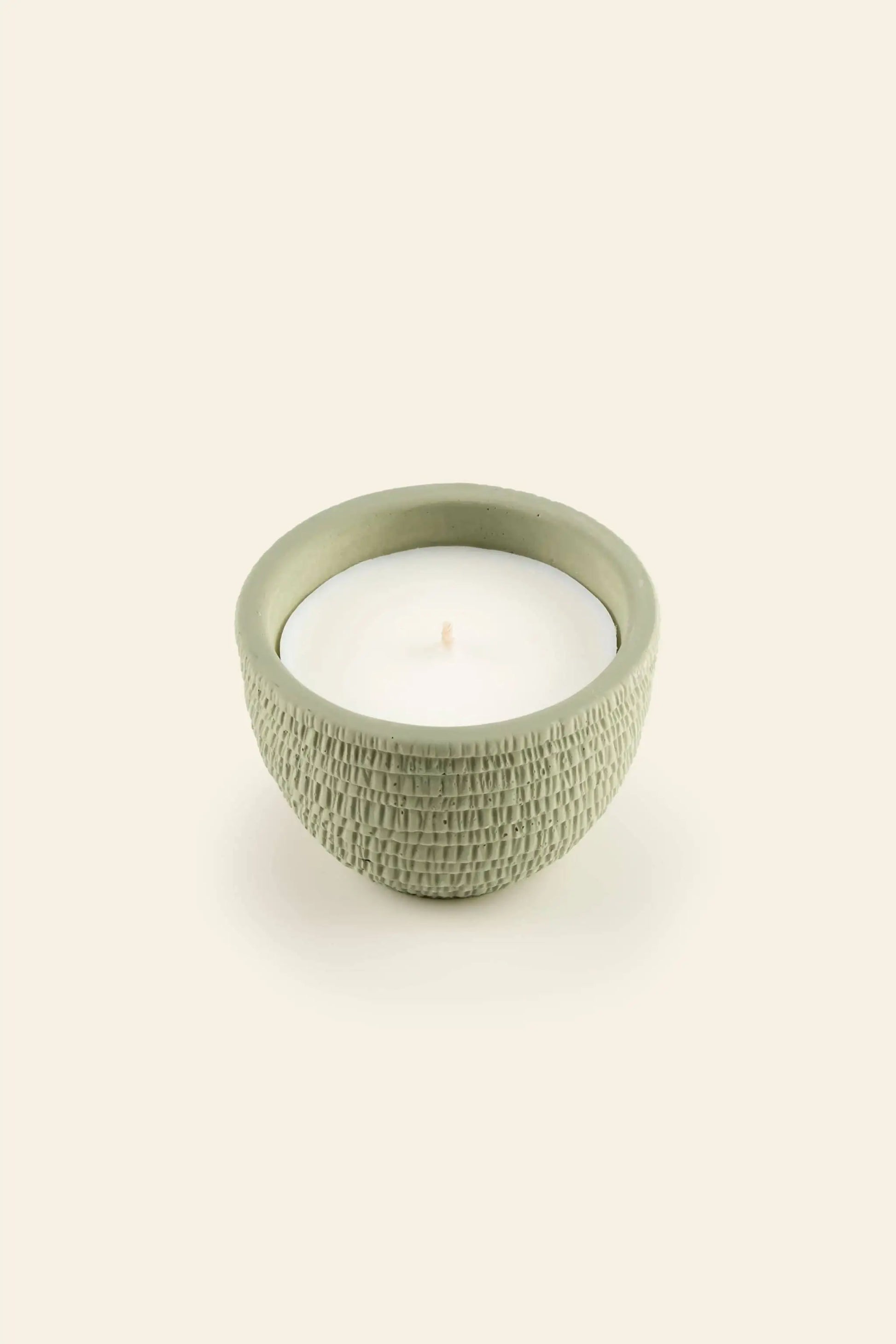 The Pass It On Alps Candle by Pass It On features a small white candle in a textured, round, light green ceramic holder with an English Pear & Freesia scent, presented against a plain beige background.