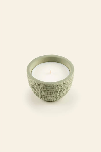 The Pass It On Alps Candle by Pass It On features a small white candle in a textured, round, light green ceramic holder with an English Pear & Freesia scent, presented against a plain beige background.