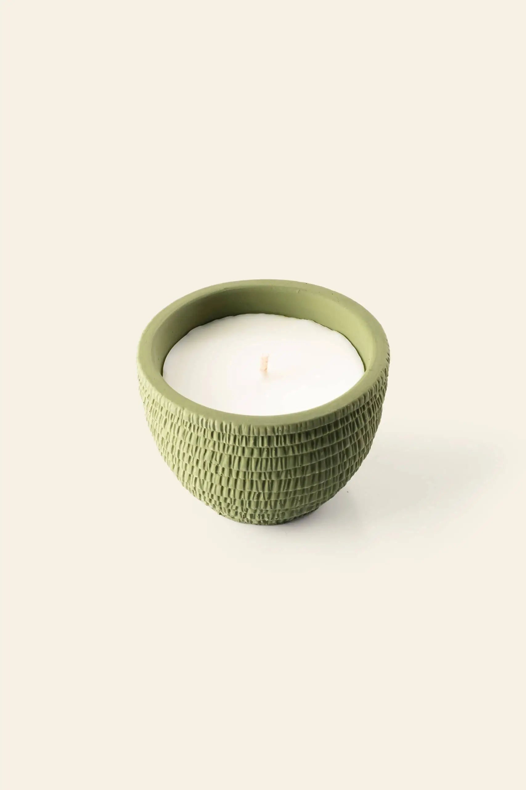 A Pass It On Amazon Candle by Pass It On, in a textured round light green ceramic bowl, sits on a plain off-white background and fills the air with its exotic fragrance.