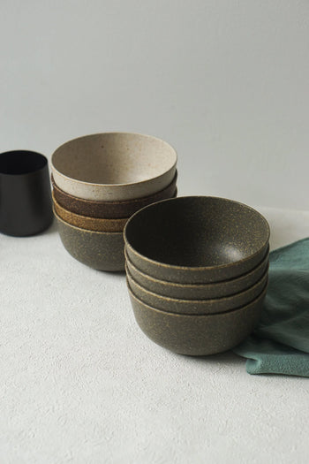 Pass It On Capsule Bowls, crafted from upcycled rice husks, sit in earthy tones on a light surface with a dark cup and green cloth nearby, highlighting Pass It On’s minimalist and sustainable design.