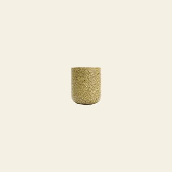 The Pass It On Capsule Cup, Rice Husk by Pass It On—a small cylindrical cup made from upcycled rice husks in mottled gold—sits centered on a plain beige background, offering an eco-conscious choice for your daily routine.