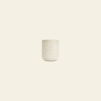 A small, round Pass It On Capsule Cup, Rice Husk by Pass It On, made from upcycled rice husks with a smooth, speckled light beige finish, is centered on a plain off-white background.