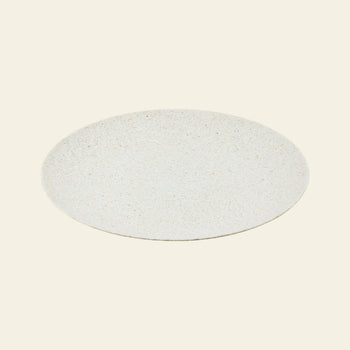 The Pass It On Dining Plate L, Rice Husk by Pass It On is a round, flat, light-speckled beige plate made from upcycled rice husks, featuring a minimalist design and smooth texture—ideal for sustainable dining on an off-white backdrop.