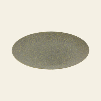 The Pass It On Dining Plate L, Rice Husk by Pass It On features a round, flat, greyish-brown design with a speckled texture—made from upcycled materials and set against an off-white background—ideal for sustainable dining.