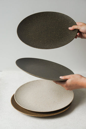Two hands stack Pass It On Dining Plate L, Rice Husk by Pass It On on a white surface, highlighting eco-friendly tableware in natural tones against a plain background.