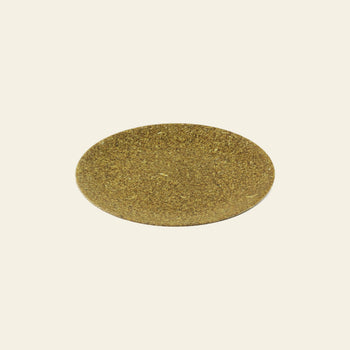 A round, flat, brownish-green Pass It On Dining Plate M, made from rice husk by Pass It On, is centered on a plain off-white background.