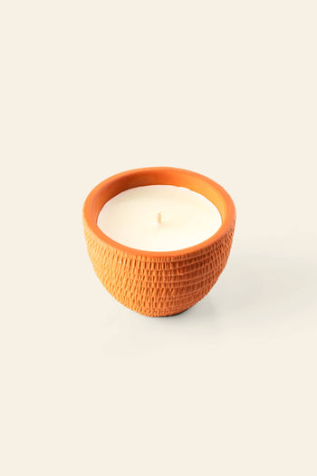 The Pass It On Taj Mahal Candle, by Pass It On, features a small white candle in a round, textured terracotta pot set against a light beige backdrop, capturing the timeless elegance of Indian culture.