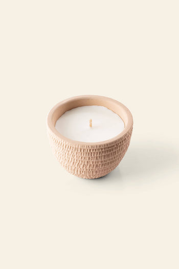 The Pass It On Venice Candle by Pass It On is a white romantic candle with patchouli and rose scent in a round, textured beige ceramic container featuring a subtle pattern and single centered wick, set against a plain light background.