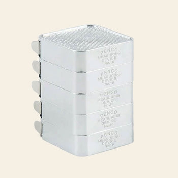 A stack of four silver rectangular metal objects labeled Penco Pocket Measure by Penco, showcasing a retro-inspired design with a textured top and small side tabs, reminiscent of a compact stainless steel measuring tape.