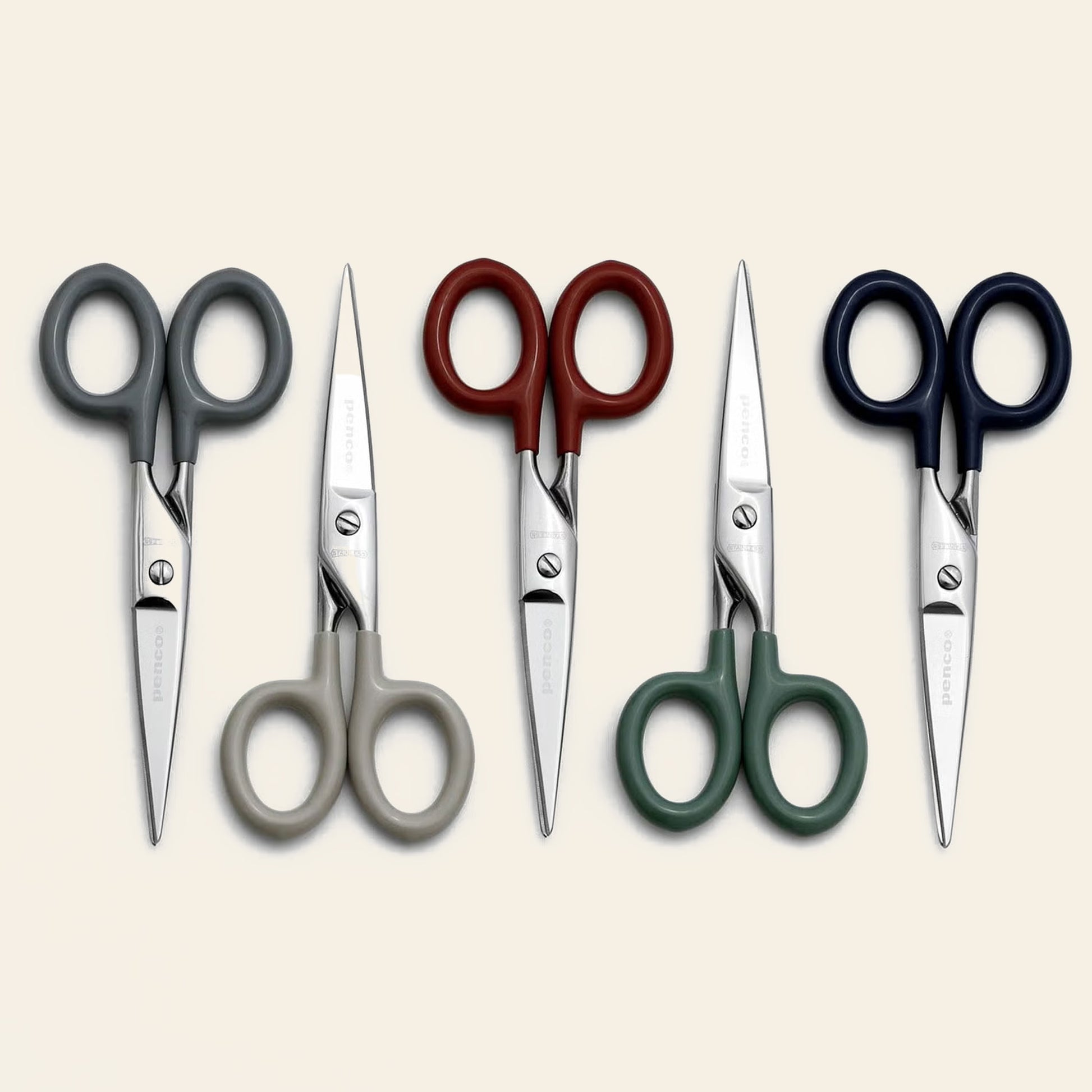 Four pairs of Penco Stainless Steel Scissors S, featuring handles in gray, beige, red, green, and navy blue, are neatly arranged side by side on a plain light background. Created by Penco, these stainless steel scissors offer everyday functionality paired with a stylish design.
