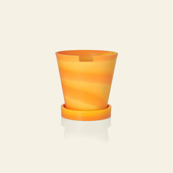The Plastic Ark Dirty Pot by Plastic Ark features an orange and yellow swirl design with a matching saucer, crafted from recycled plastic, shown against a plain light beige background.