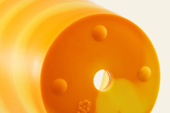 Close-up of the rounded bottom of the Plastic Ark Dirty Pot by Plastic Ark, made from orange plastic with a central hole, three raised circular bumps, and a recycling symbol.