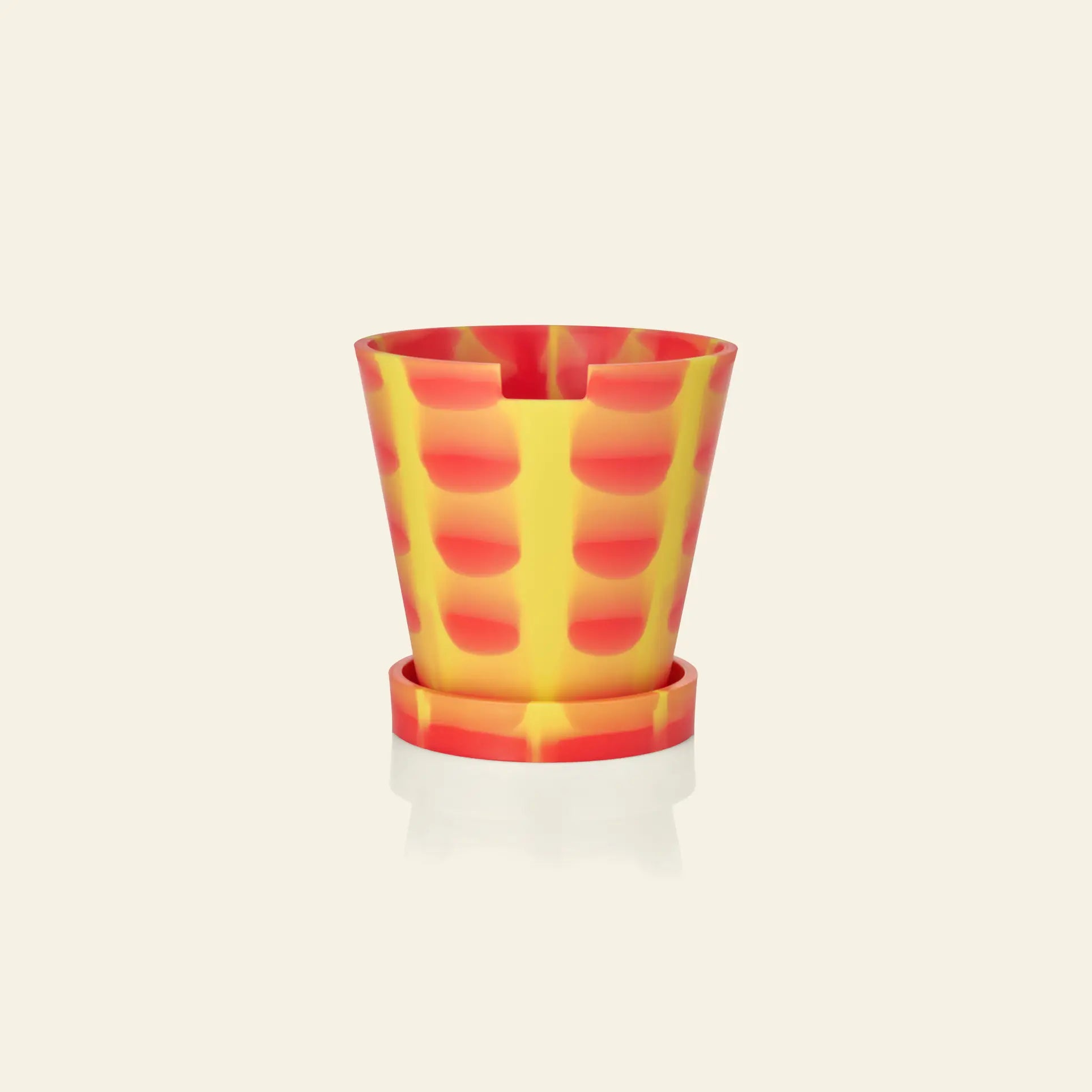 The Plastic Ark Dirty Pot by Plastic Ark is a sustainable, colorful plant pot with a matching saucer, featuring a yellow base and an abstract red checkered pattern, displayed against an off-white background.