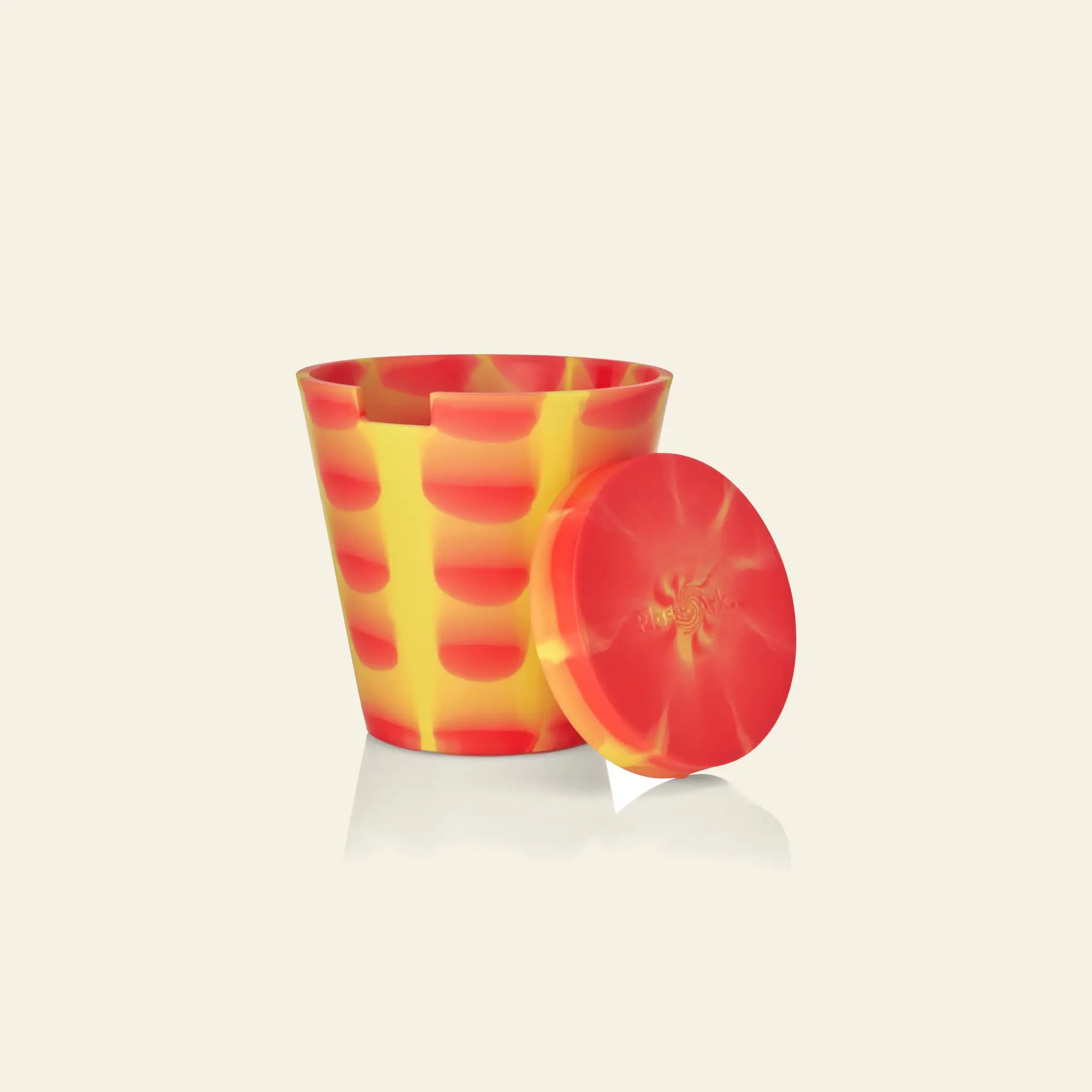 The Plastic Ark Dirty Pot by Plastic Ark is a yellow and red marbled cup with abstract patterns, displayed with its matching circular lid on its side against a plain light background.