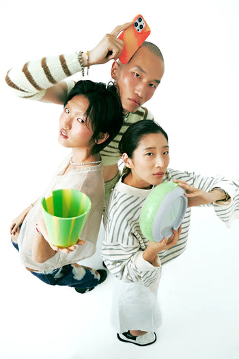 Three stylish young adults pose against a white background, confidently holding Plastic Ark Dirty Pots by Plastic Ark and a phone. They wear trendy, casual outfits in neutral and striped patterns.