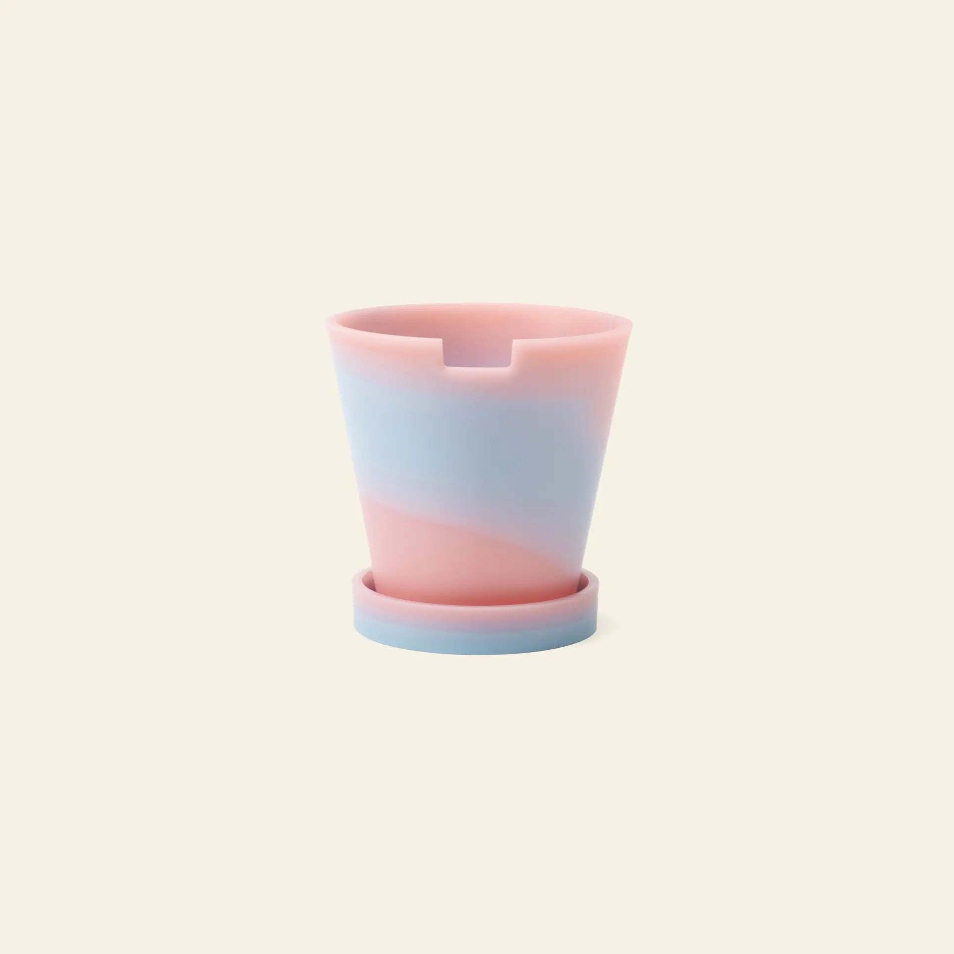 The Plastic Ark Dirty Pot by Plastic Ark is a small marbled plant pot with a matching saucer, featuring pastel pink and blue swirls, set against a plain beige background.
