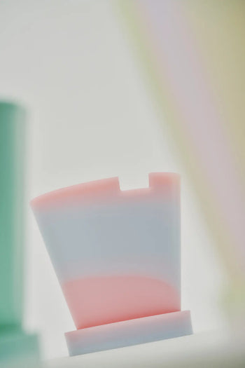 The Plastic Ark Dirty Pot by Plastic Ark features pink and light blue pastel marbling with a notched top, shown against a soft, blurred background.