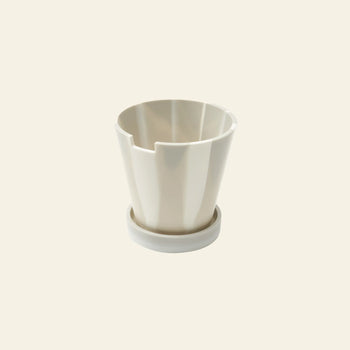 The Plastic Ark Dirty Pot by Plastic Ark is a white, modern recycled plastic planter with vertical grooves, paired with a matching round saucer and shown against a plain light beige background.