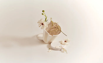 A Plastic Ark Dirty Pot by Plastic Ark lies on its side with its lid off, surrounded by delicate white flowers and sprigs on a minimal light background—perfect inspiration for displaying this unique sustainable plant pot.