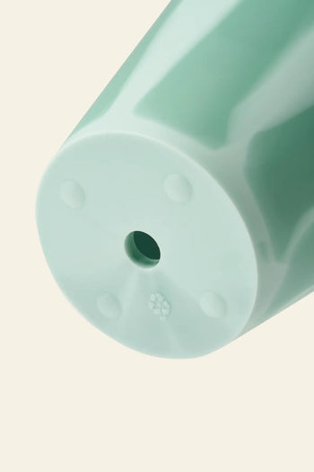 Close-up of the bottom of a Plastic Ark Dirty Pot by Plastic Ark, made from light green recycled plastic with a central hole and embossed recycling symbol, shown against a plain beige background.