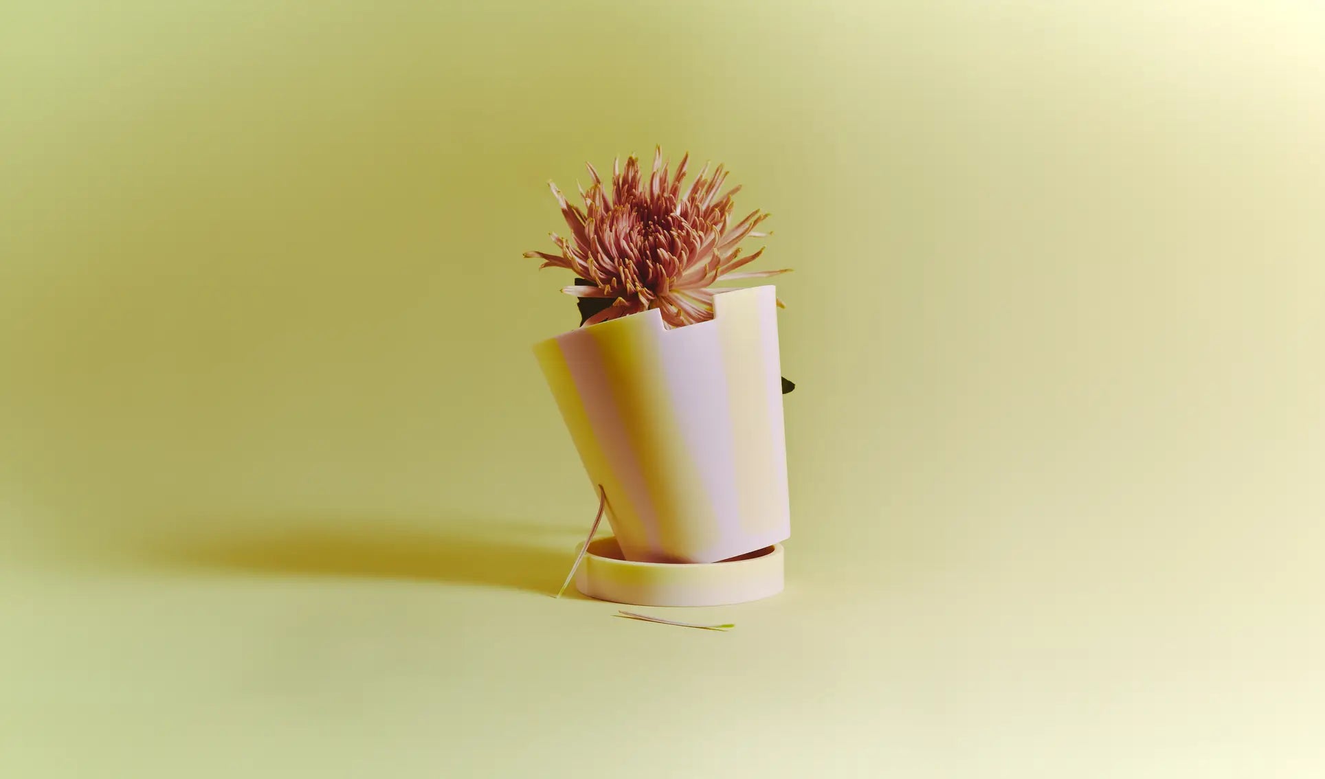 A wilted pink flower in the Plastic Ark Dirty Pot by Plastic Ark, made from recycled plastic, sits tilted against a pale yellow background with a fallen petal and leaf nearby, subtly highlighting sustainability.
