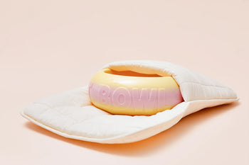 The Plastic Ark Fat Bowl by Plastic Ark, in pastel pink and yellow with BOWL embossed, rests partially wrapped in a padded white cloth on a soft beige background; made from recycled plastic for sustainability.