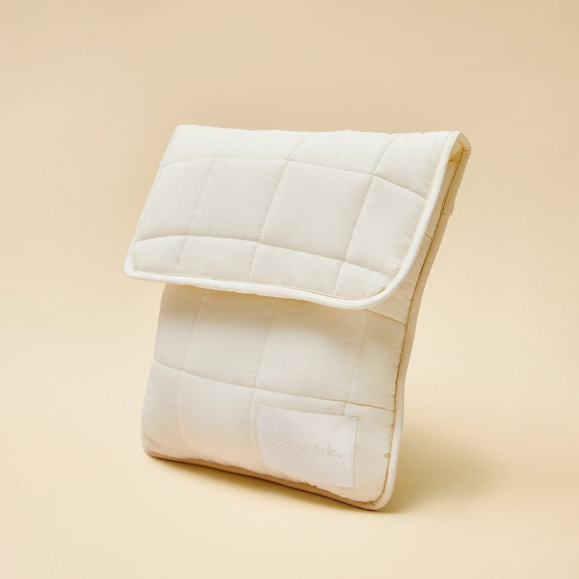 The Plastic Ark Fat Bowl by Plastic Ark is a rectangular, cream-colored, quilted pouch with a flap closure and modular design. Displayed upright on a beige background, it has a subtle stitched label on the front.