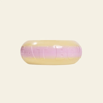 The Plastic Ark Fat Bowl by Plastic Ark is a chunky, round recycled plastic bangle with a gradient from pale yellow to light pink, featuring raised blocky letters on its surface.