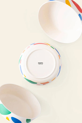 Three Poketo Bamboo Bowls with colorful abstract patterns by Poketo are arranged on a light beige surface; two shown from the side and one upside down, displaying the Poketo logo—ideal for sustainable outdoor dining.