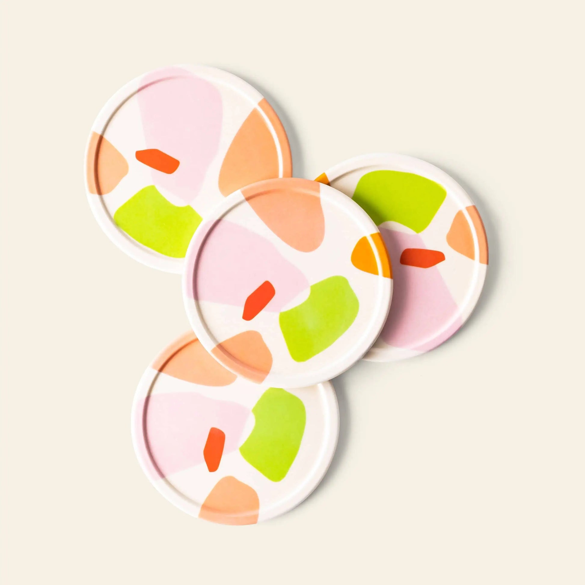 The Poketo Bamboo Coasters, Set of 4, feature abstract patterns in pink, orange, green, and red on a light background. Arranged overlapping on a cream surface, these eco-friendly coasters are made from durable bamboo fibres.
