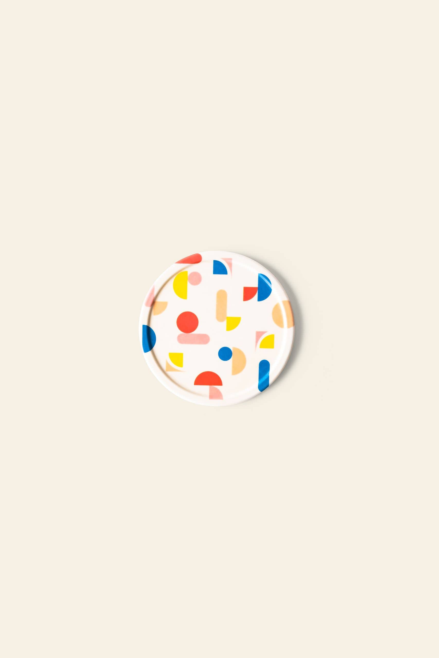 The Poketo Bamboo Coasters, Set of 4, feature colorful geometric shapes in red, yellow, blue, and pink on a round white surface, adding a vibrant touch to any tabletop display.