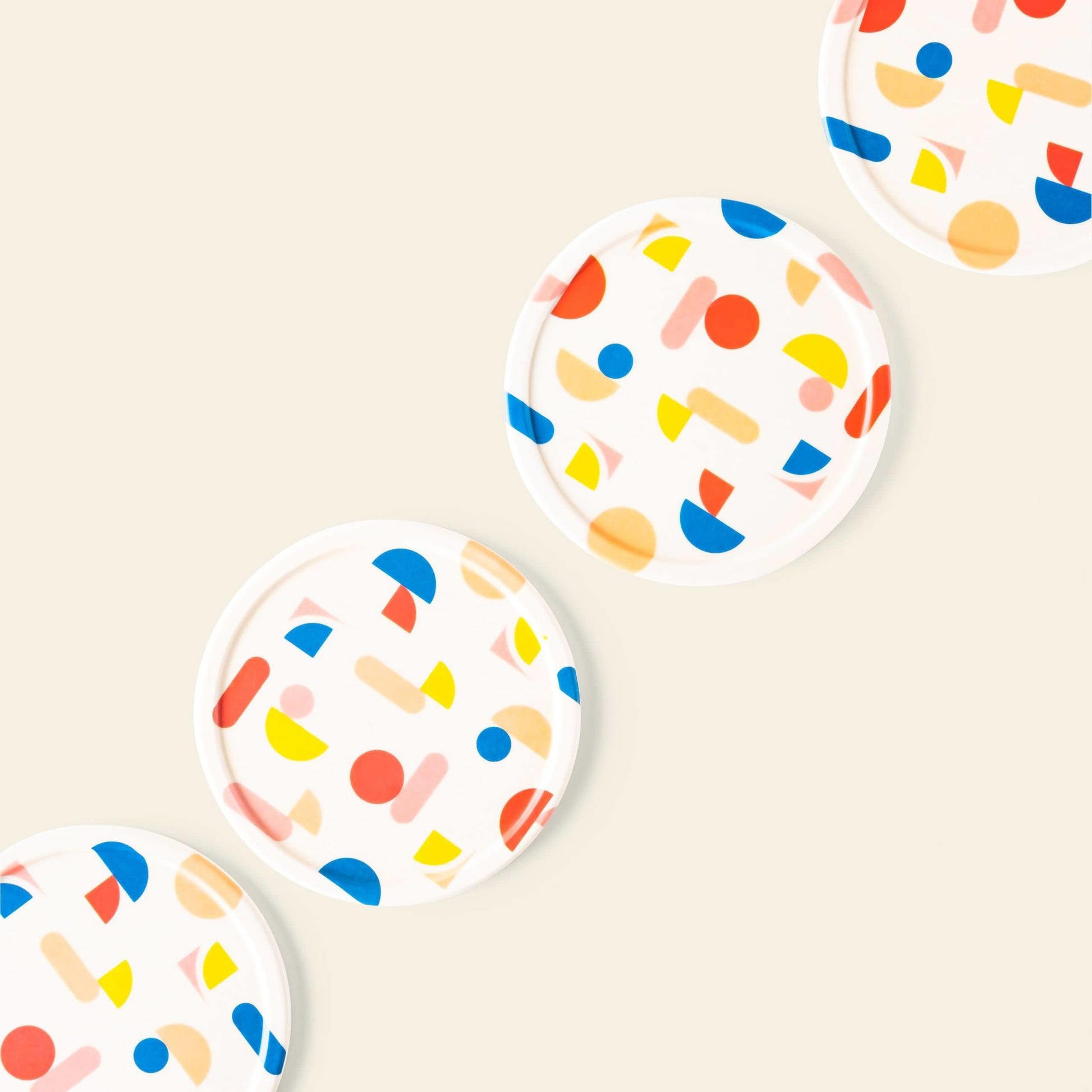 The Poketo Bamboo Coasters, Set of 4, feature colorful abstract shapes in blue, red, yellow, and orange and are arranged diagonally on a light beige tabletop background.