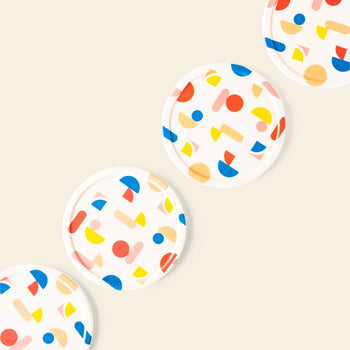 The Poketo Bamboo Coasters, Set of 4, feature colorful abstract shapes in blue, red, yellow, and orange and are arranged diagonally on a light beige tabletop background.