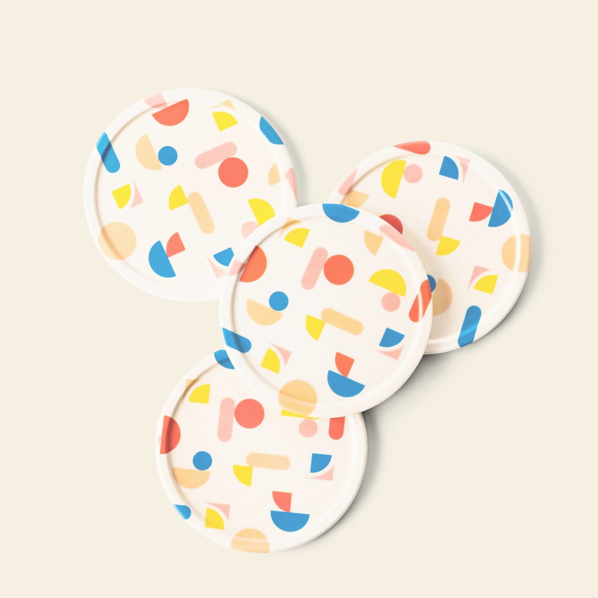 The Poketo Bamboo Coasters, Set of 4, are crafted from bamboo fibres and display a colorful abstract pattern of red, yellow, and blue geometric shapes on a white background—perfect for brightening your tabletop.