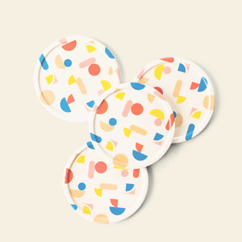 The Poketo Bamboo Coasters, Set of 4, are crafted from bamboo fibres and display a colorful abstract pattern of red, yellow, and blue geometric shapes on a white background—perfect for brightening your tabletop.