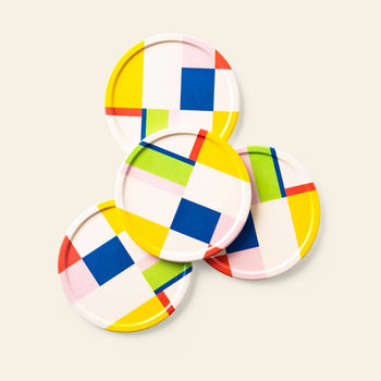 The Poketo Bamboo Coasters, Set of 4, feature bold geometric patterns in yellow, pink, blue, red, and green on white—perfect for adding flair to your tabletop.