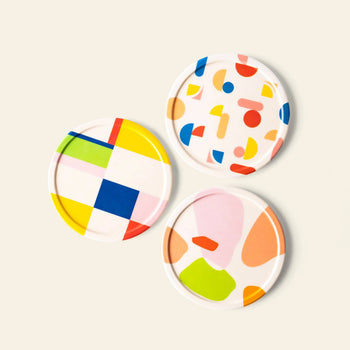 Poketo Bamboo Coasters, Set of 4, feature colorful abstract patterns: geometric squares and stripes, multicolored shapes on white, and large pastel accents. Made from bamboo fibers and displayed against a plain light background.