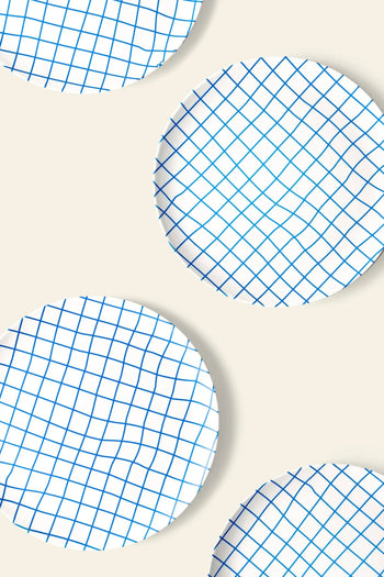 Four Poketo Bamboo Dinner Plates by Poketo, featuring a blue grid pattern, are arranged diagonally on a beige background with some plates extending past the edges—ideal for adding style to any dinner party.