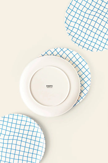 Three round plates on a light background: two with blue grid patterns and one plain white Poketo Bamboo Dinner Plate in the center, showing the Poketo brand—perfect for eco-friendly dinner parties.