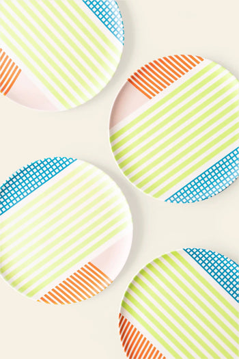 Four Poketo Bamboo Salad Plates by Poketo, featuring white surfaces with green stripes, orange lines, and blue grid patterns, are arranged on a light surface. The eco-friendly plates overlap slightly and sit at various angles.