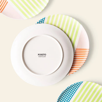 Three Poketo Bamboo Salad Plates with colorful stripes in pink, green, orange, and blue are arranged on a light surface. The center plate is upside down, revealing the Poketo brand—perfect for stylish and sustainable dining.