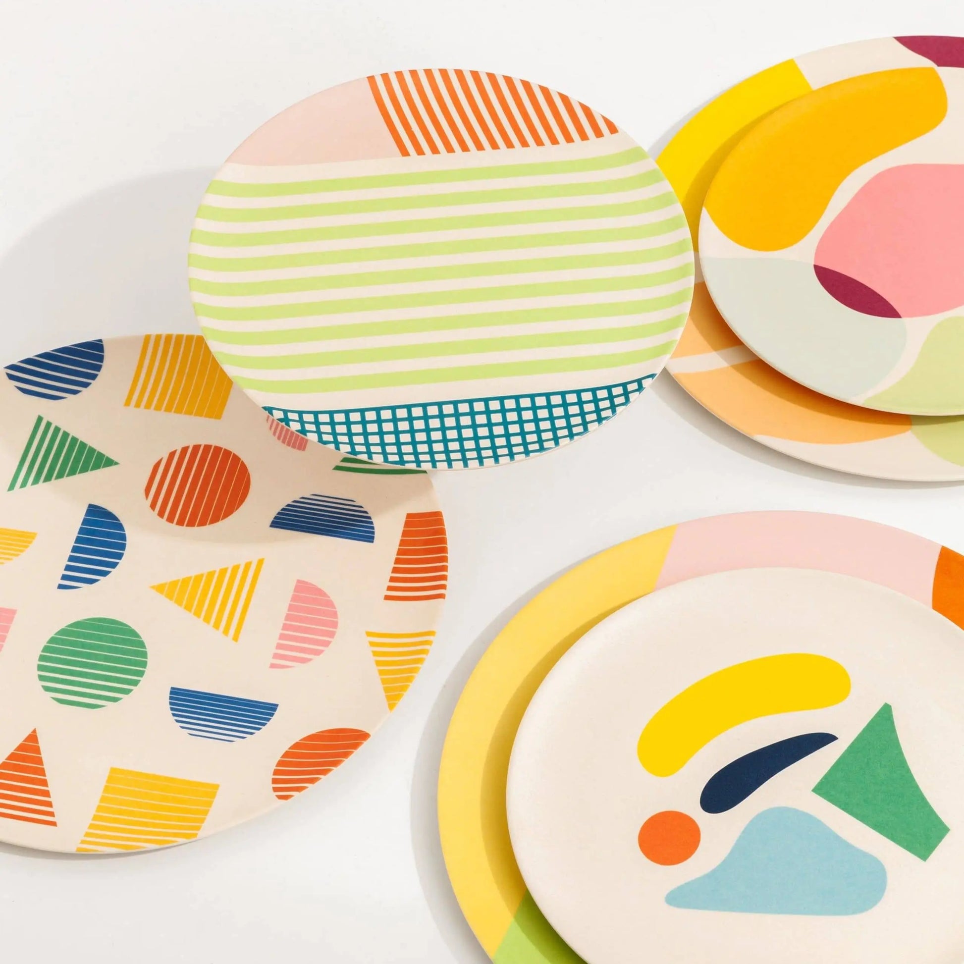 Poketo Bamboo Salad Plates by Poketo feature abstract patterns—stripes, geometric shapes, and organic designs—in vibrant yellow, pink, blue, green, and orange. These eco-friendly plates overlap on a clean white background for a lively tablescape.