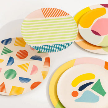 Poketo Bamboo Salad Plates by Poketo feature abstract patterns—stripes, geometric shapes, and organic designs—in vibrant yellow, pink, blue, green, and orange. These eco-friendly plates overlap on a clean white background for a lively tablescape.