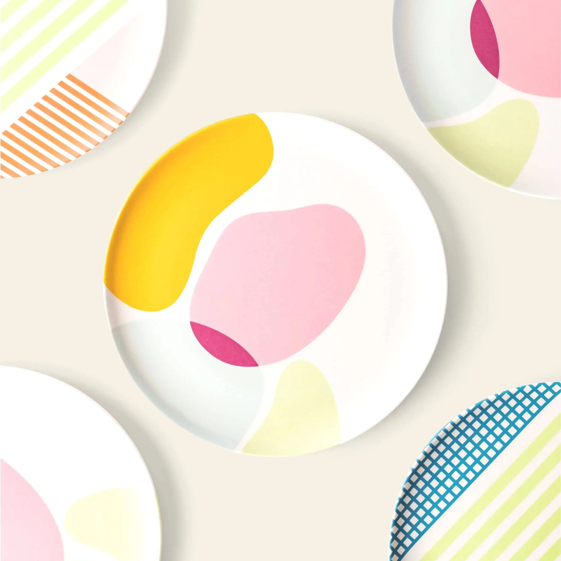 The Poketo Bamboo Salad Plate by Poketo features eco-friendly round plates with abstract pastel patterns—yellow, pink, blue, and green shapes with stripes or grids—perfect for sustainable dining on any table.